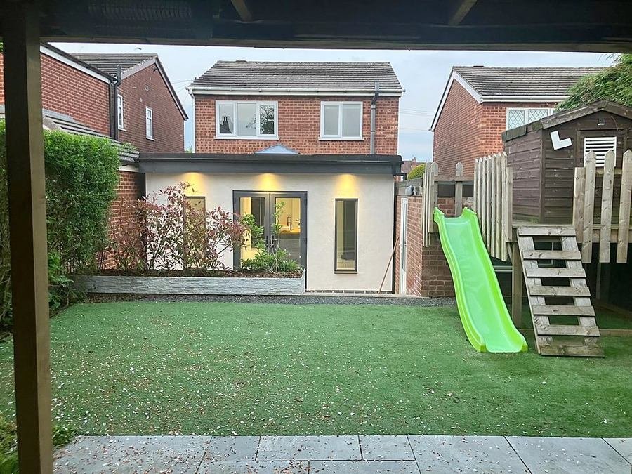 Rear extension lit from inside at dusk with the garden laid to lawn