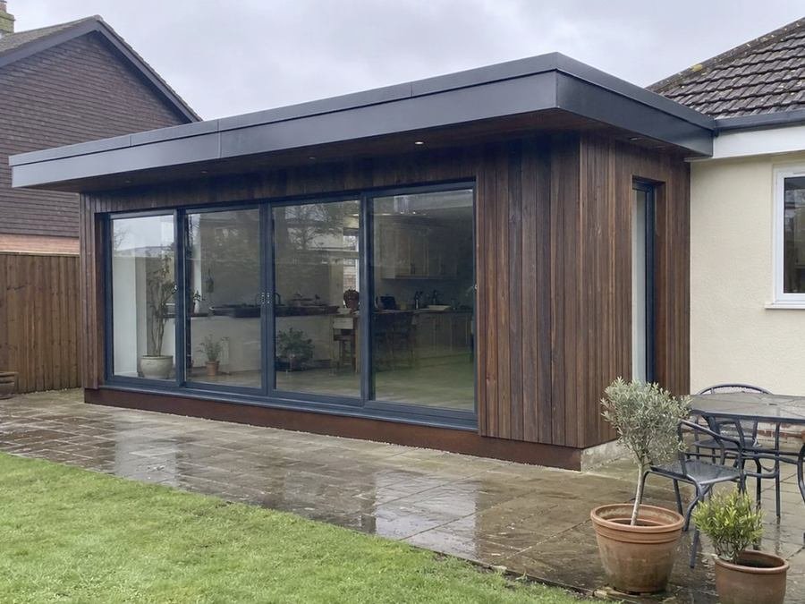 Timber clad garden room with full width sliding doors onto a patio
