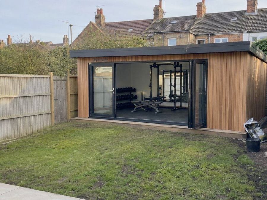 Timber clad garden room in use as a home gym with bifold doors open